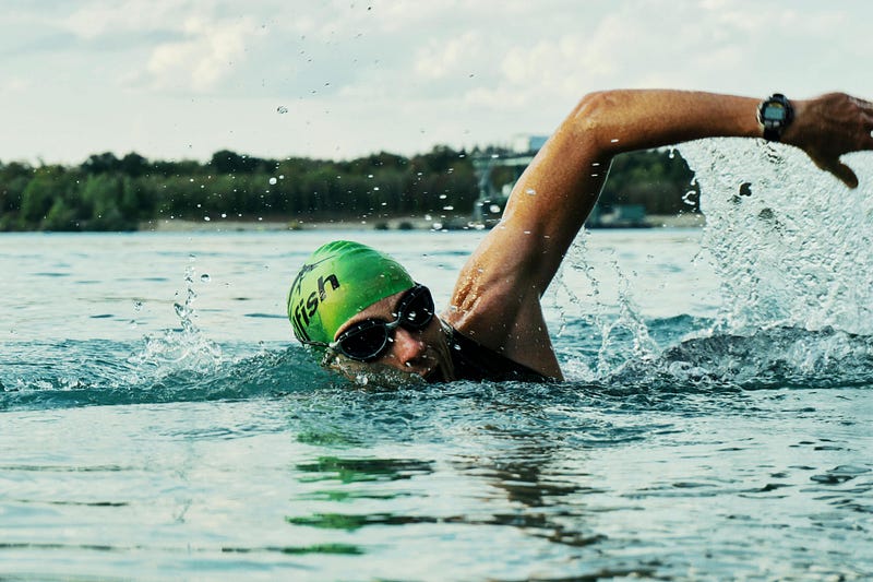 A man half-way through a best stroke in blue water rotating his arm outside of the water and getting ready to take a breath.