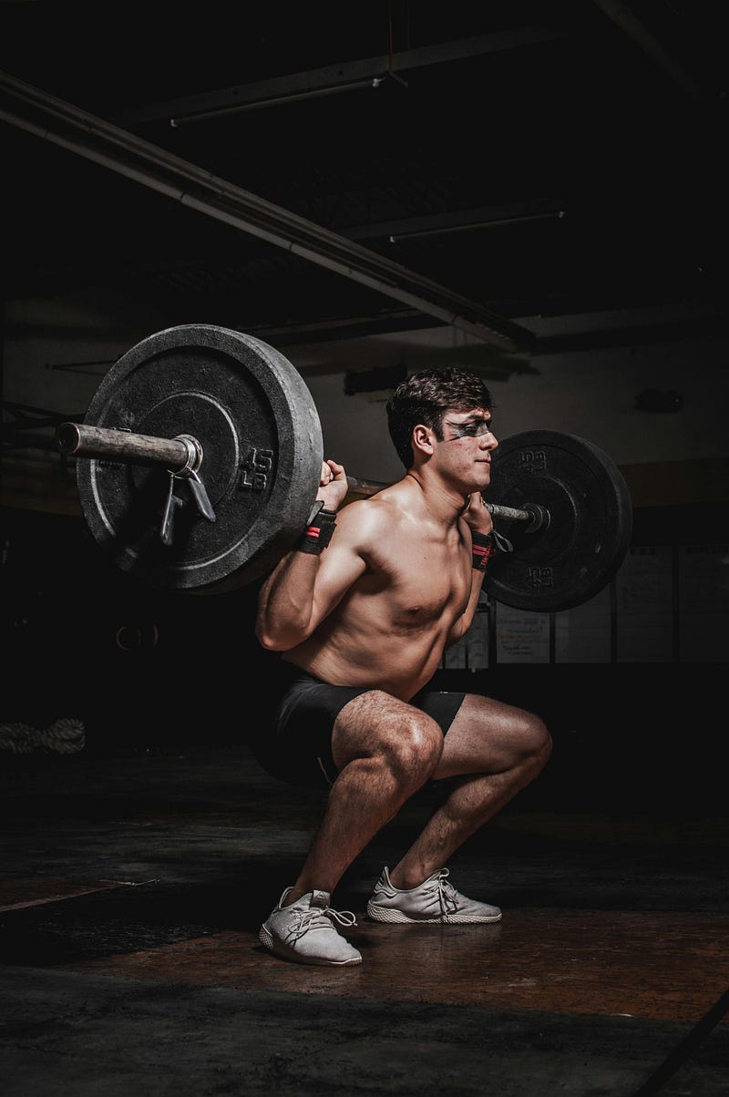 A strong man concentrating on standing up from a deep squat with a loaded bar with heavy weights on each end.